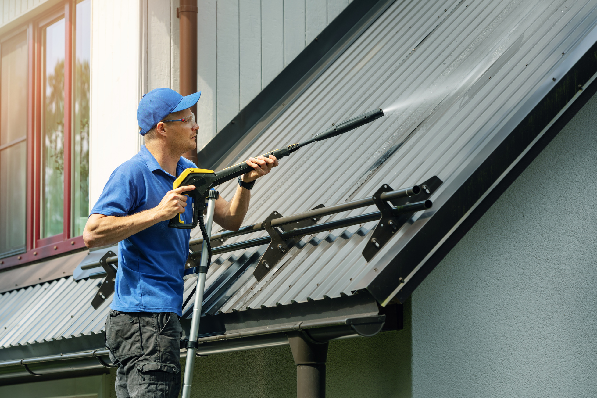 man standing on ladder and cleaning house metal roof with high pressure washer